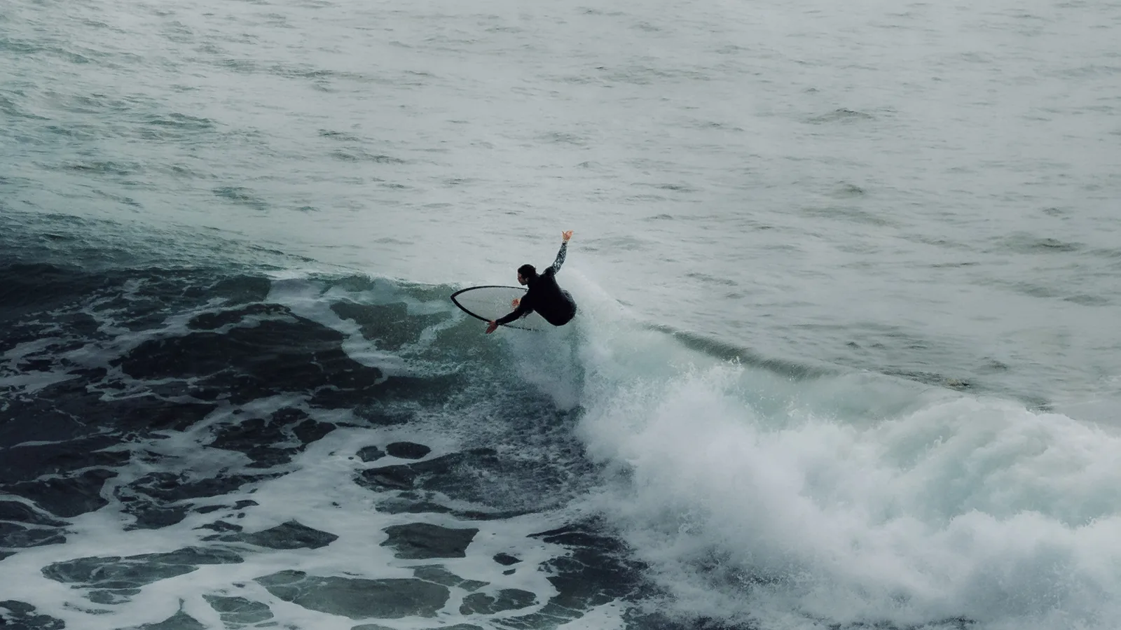 Surfer slashing off the lip of a dark wave under overcast skies off Essaouira, Morocco