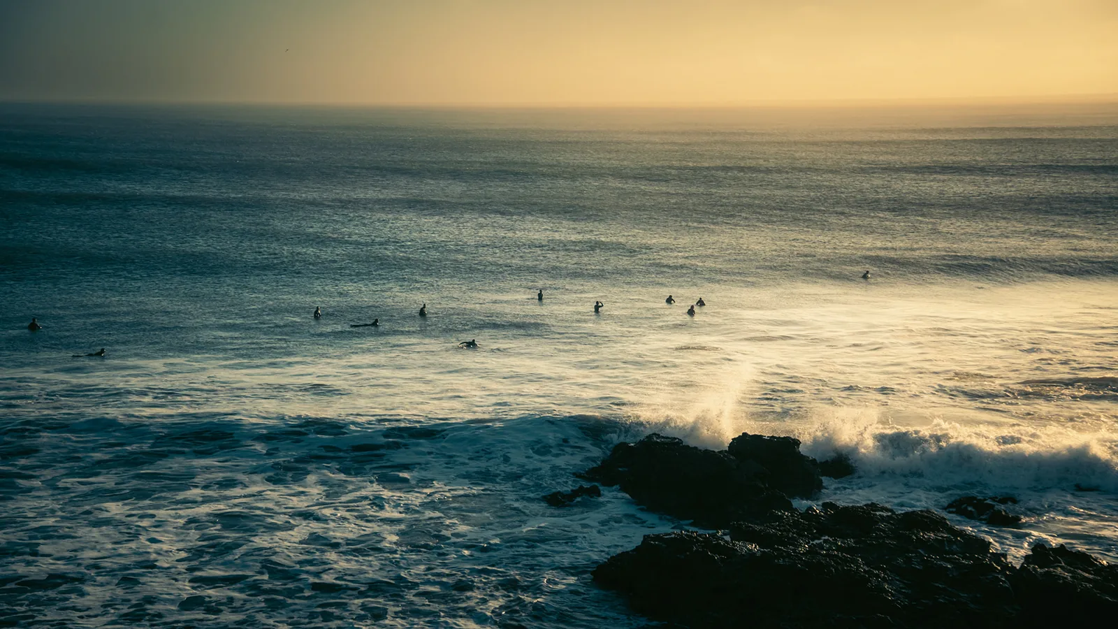Group of surfers bobbing in a sunlit lineup beyond crashing rocky shorebreak in Essaouira, Morocco