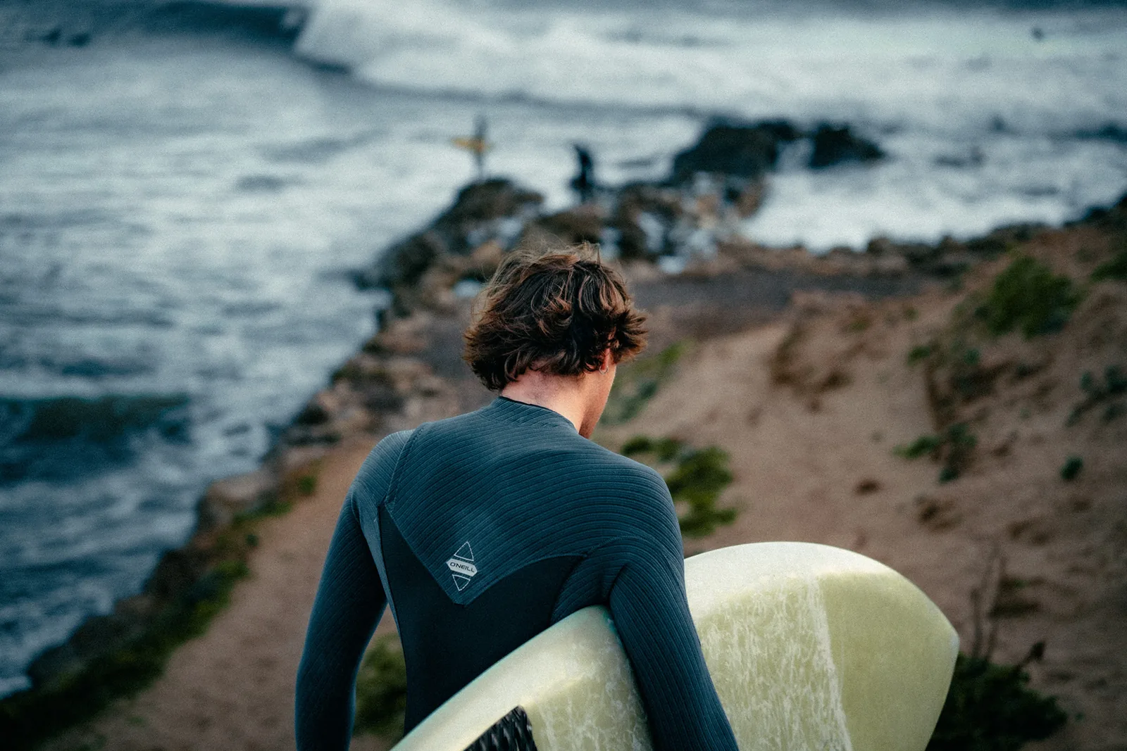 Surfer pausing on a rocky point to scan the incoming swell in Essaouira, Morocco
