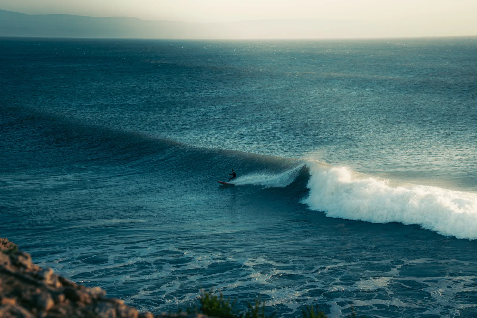 Silhouetted surfer riding a long wave face at dusk off the coast of Essaouira, Morocco