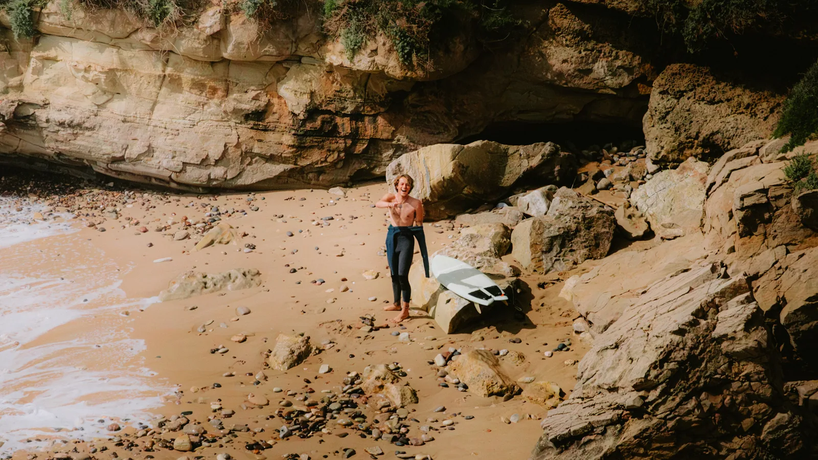 Surfer standing among boulders on a secluded cove beach in Essaouira, Morocco