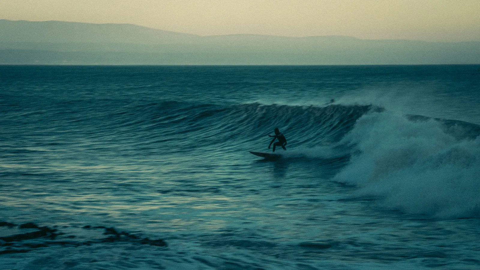 Surfer riding a wave with hazy hills lining the horizon near Essaouira, Morocco