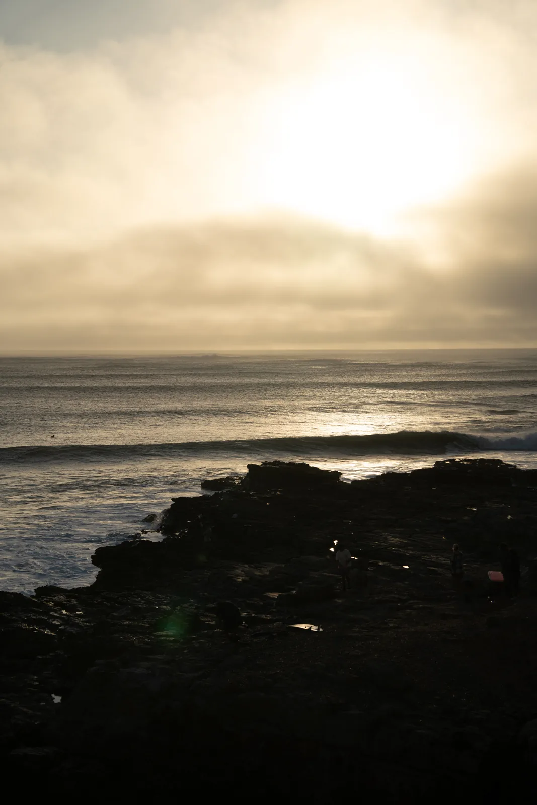 Hazy sun breaking through clouds over a rocky shoreline in Essaouira, Morocco