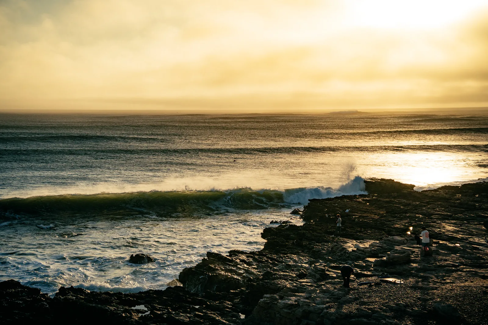 Golden sunset glow over crashing waves and dark tide pools in Essaouira, Morocco