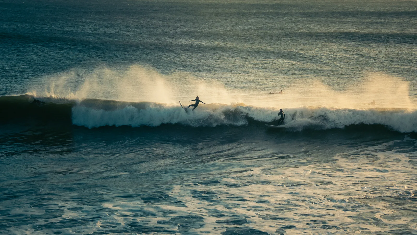 Two surfers riding the same breaking wave through spraying whitewater off Essaouira, Morocco