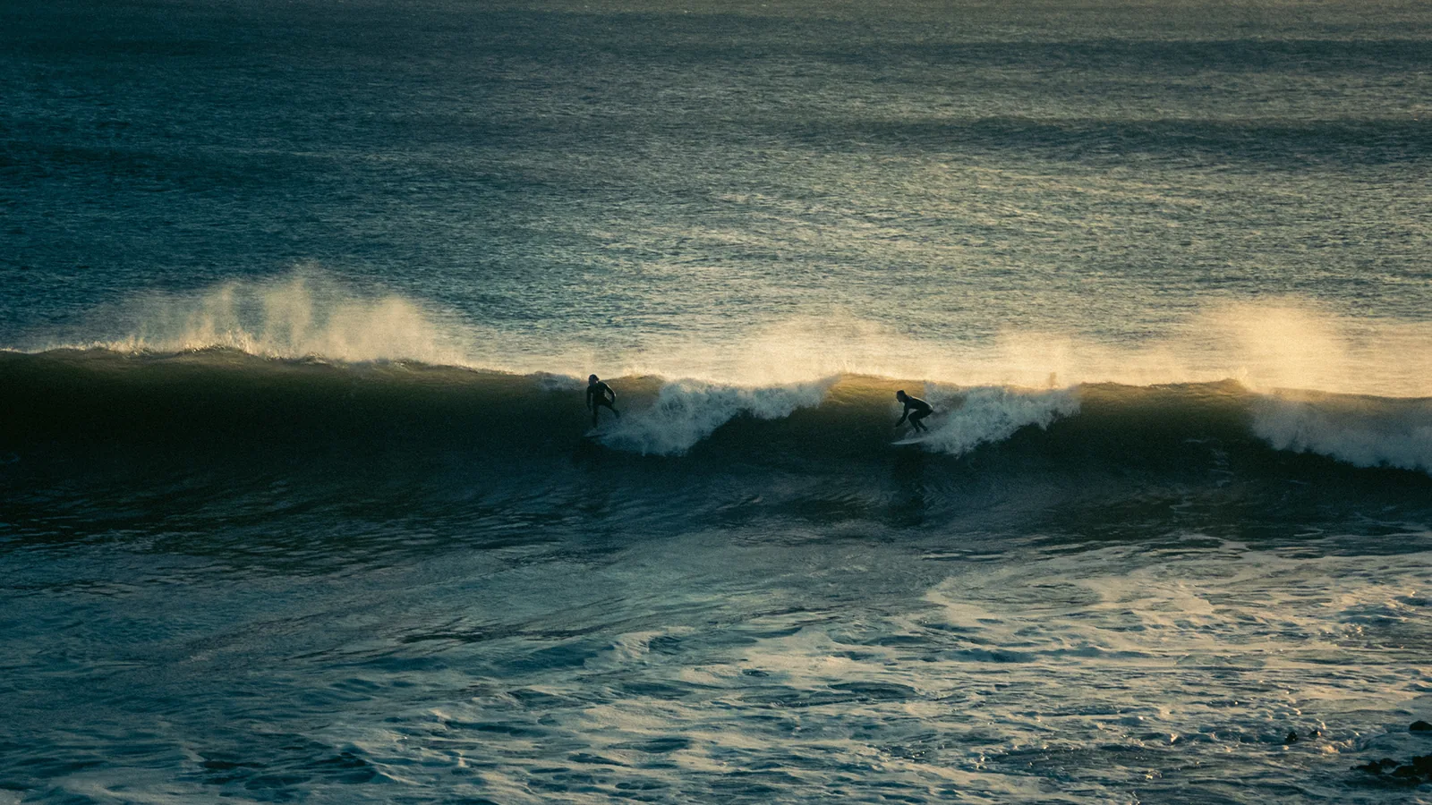 Pair of surfers gliding side by side along a glassy wave off Essaouira, Morocco