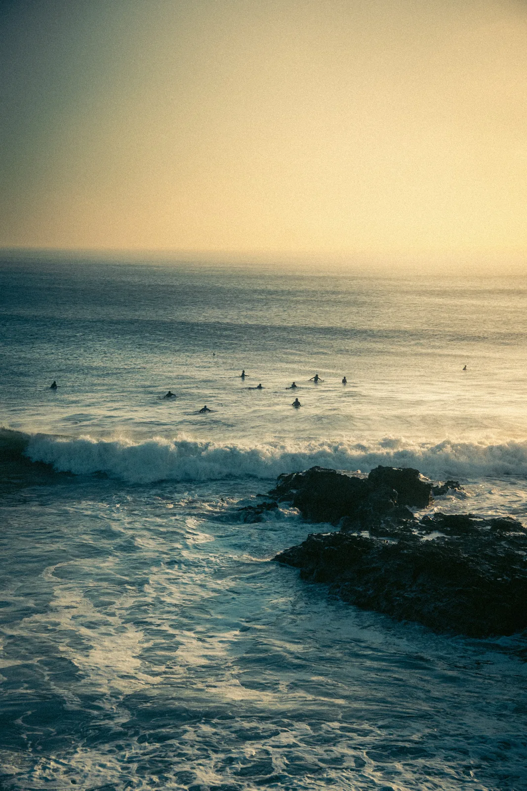 Silhouetted surfers waiting in a hazy lineup beyond the rocky shoreline in Essaouira, Morocco