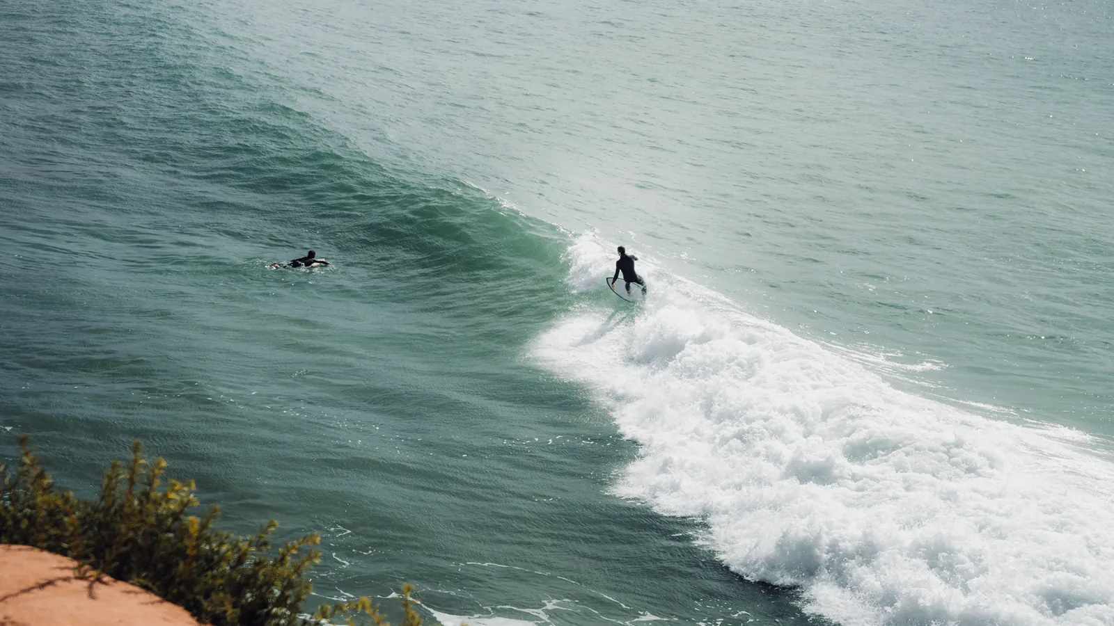 Two surfers sharing a breaking wave, one paddling and one carving, off Essaouira, Morocco