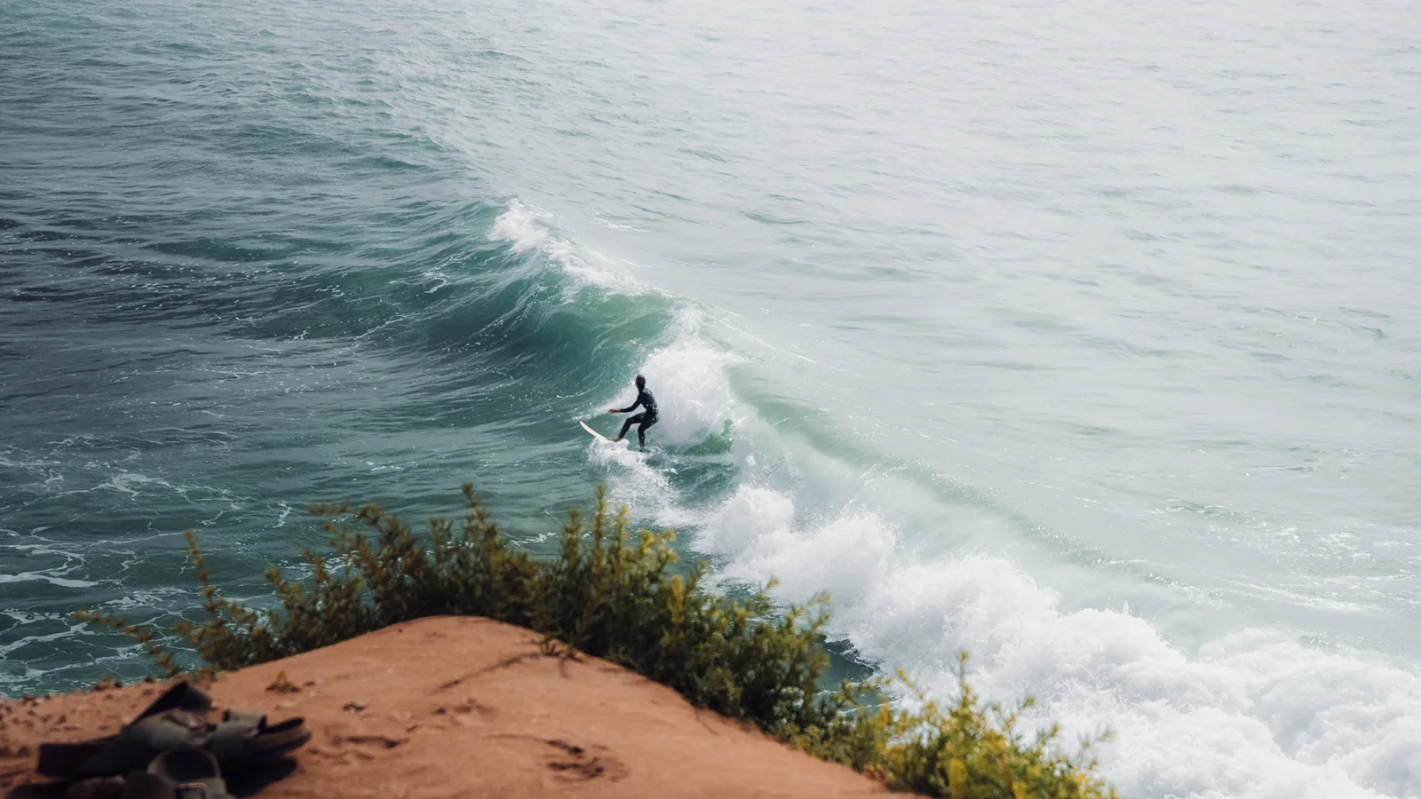 Surfer dropping into a clean wave viewed from a sandy clifftop above Essaouira, Morocco