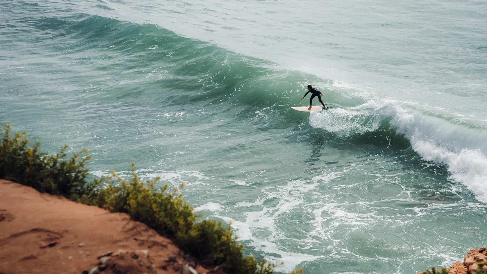 Surfer angling down the line of a green wave beside coastal cliffs in Essaouira, Morocco