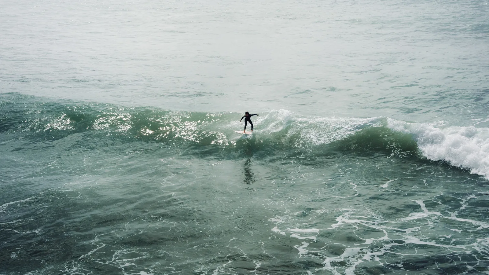 Surfer balancing arms wide atop a foamy wave crest off Essaouira, Morocco