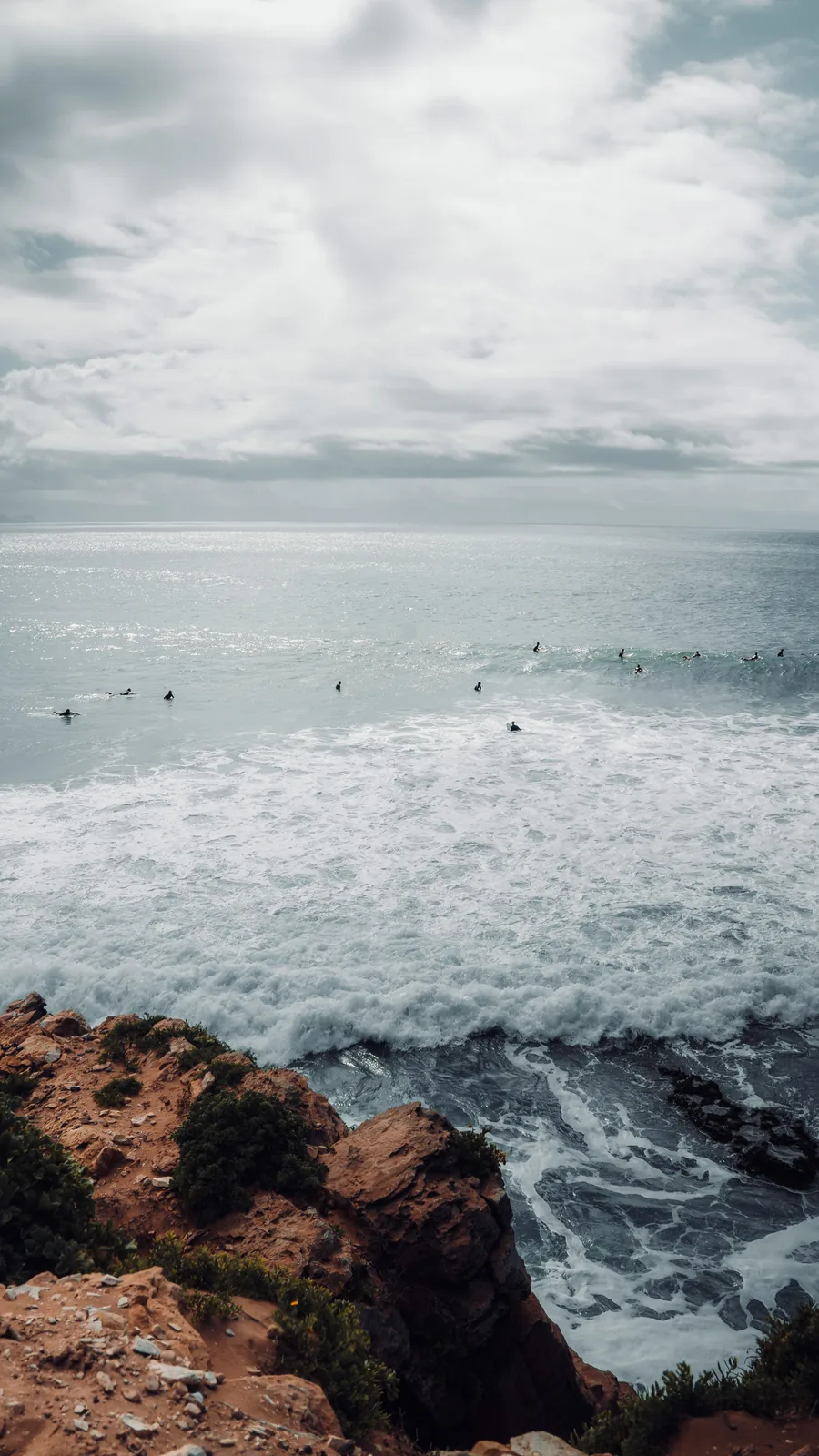 Cliffside view of surfers scattered across a stormy grey lineup in Essaouira, Morocco