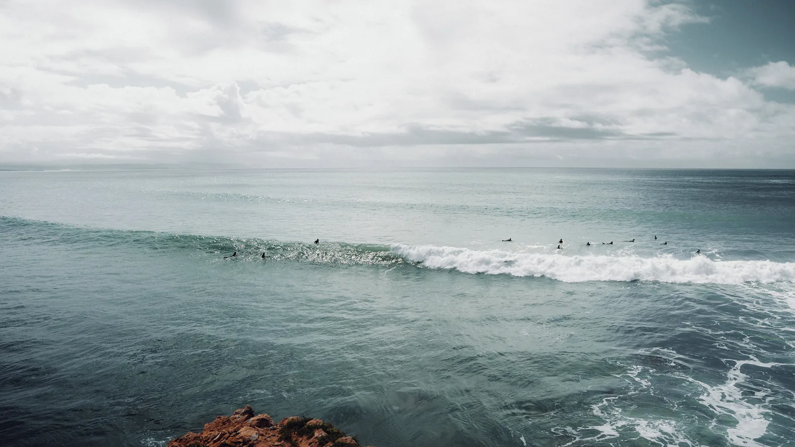Wide view of a surf lineup beneath heavy clouds along the cliffs of Essaouira, Morocco