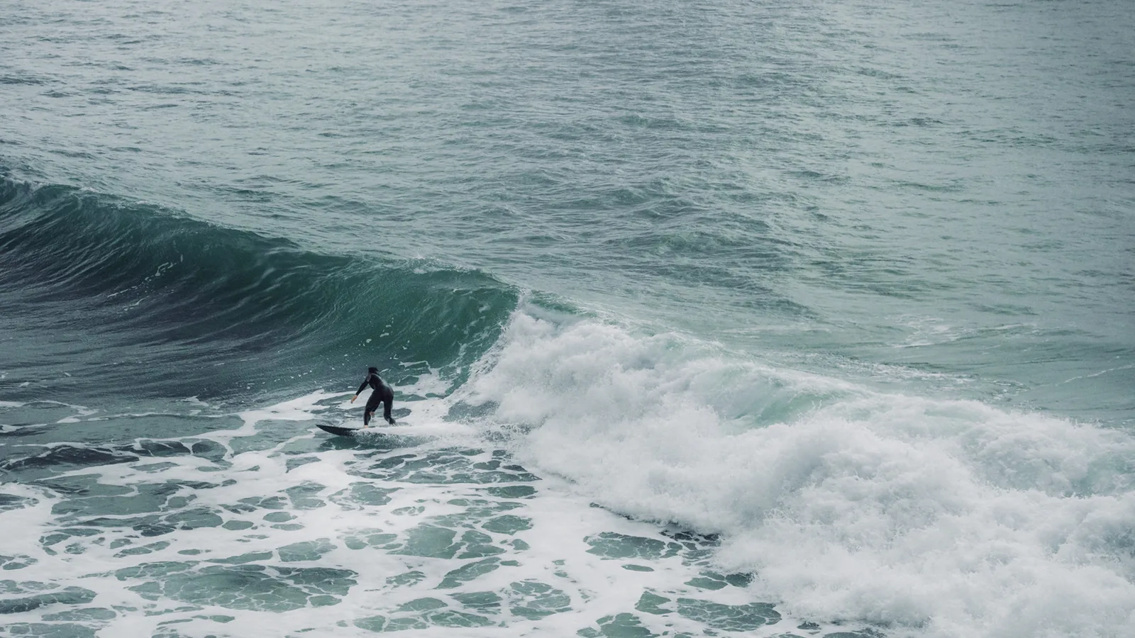 Surfer riding a smaller wave beneath overcast skies near Essaouira, Morocco