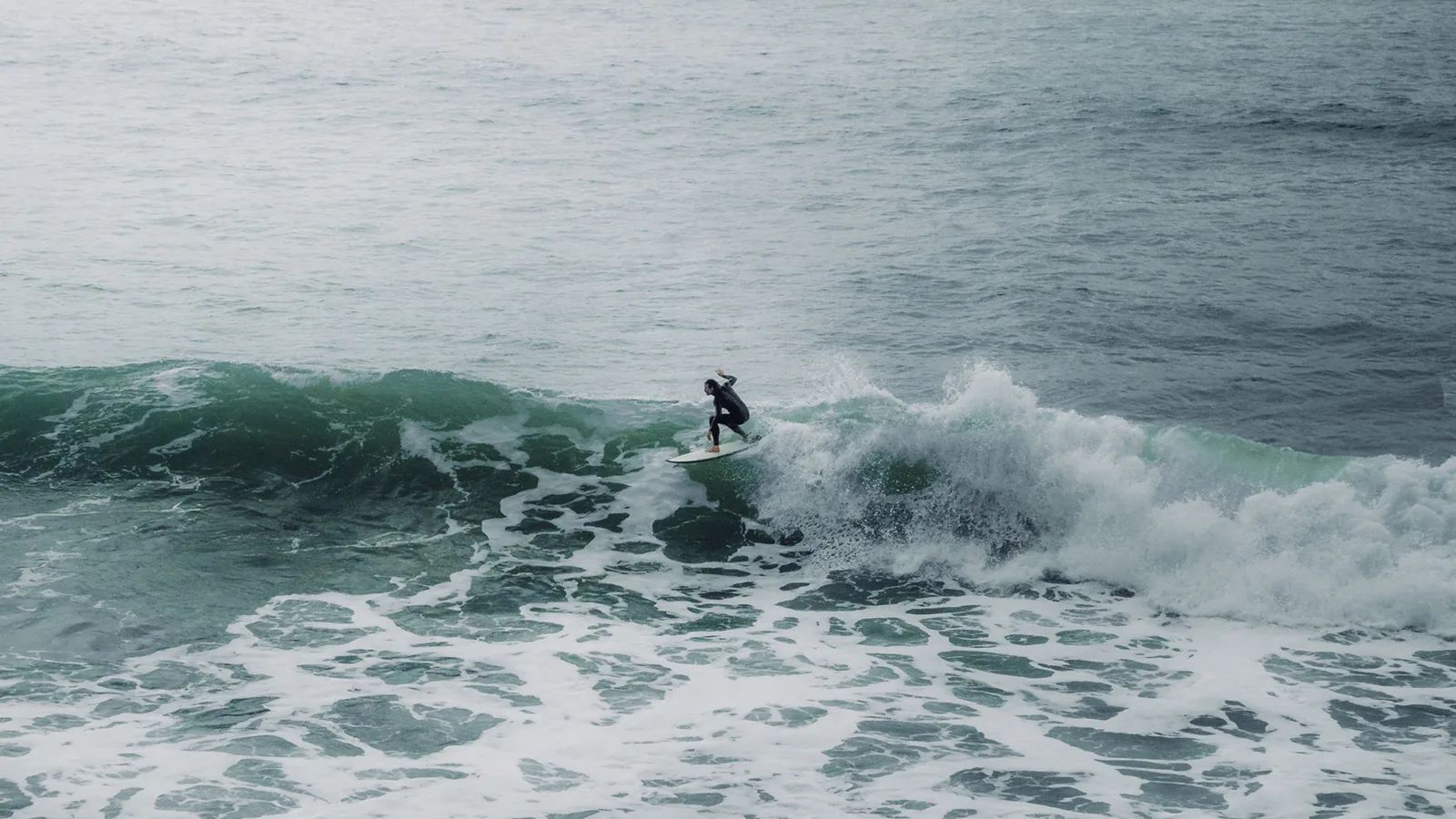 Surfer gliding across a small wave under a hazy grey sky in Essaouira, Morocco