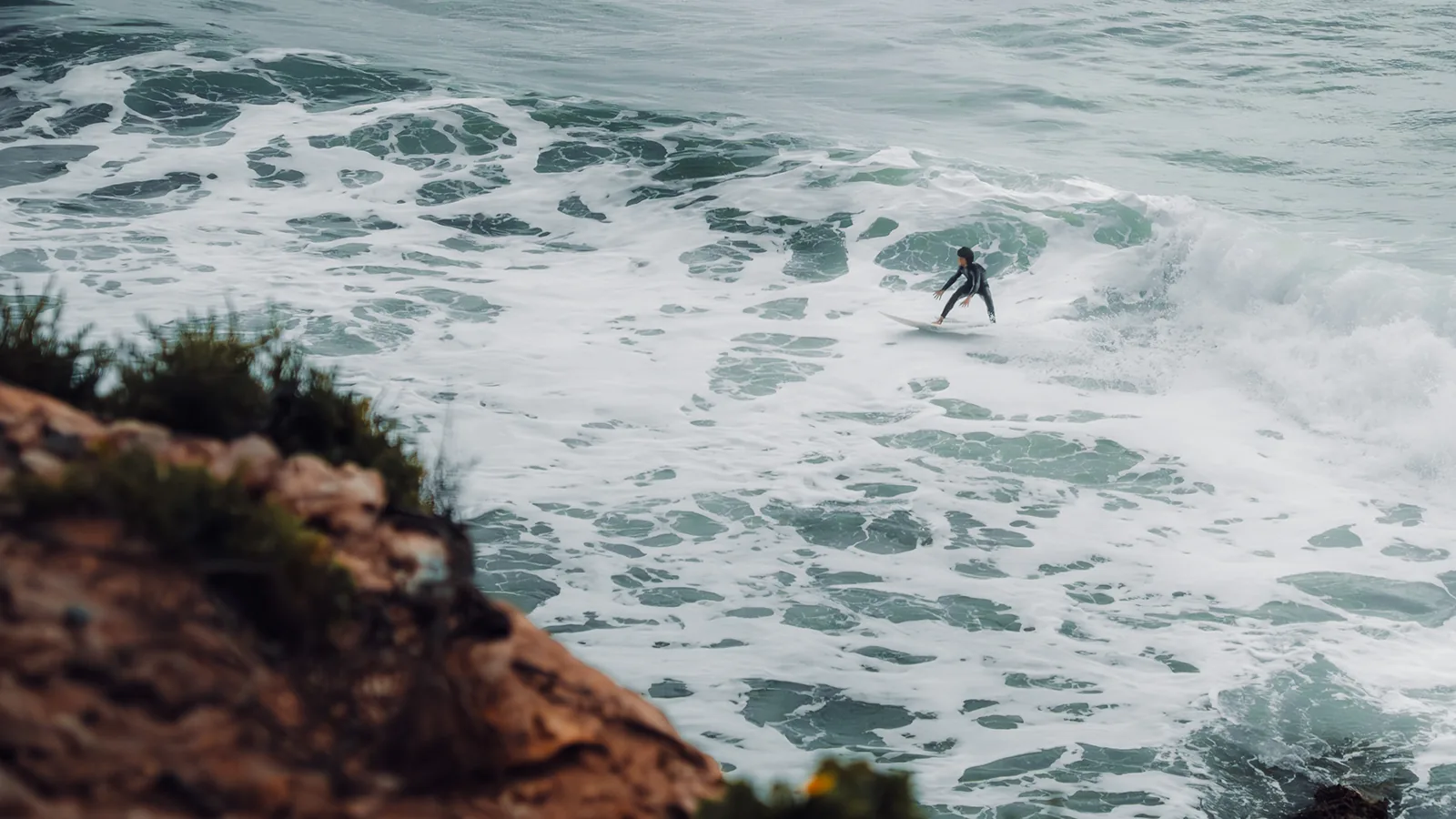 Surfer balancing through a burst of whitewater seen from a rocky clifftop in Essaouira, Morocco