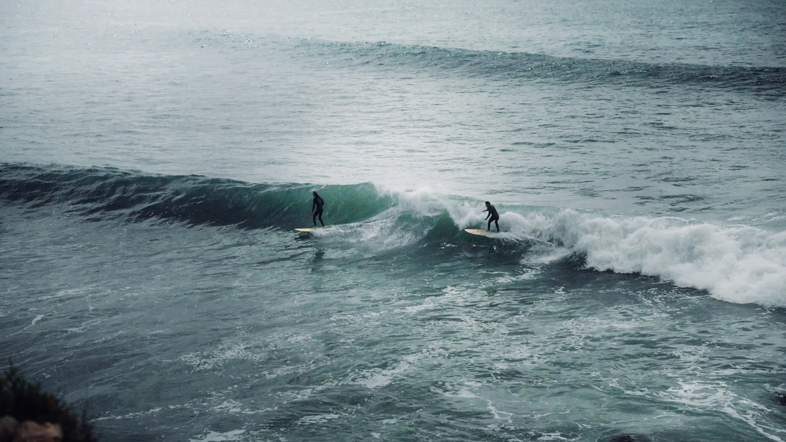 Two surfers glide down parallel green waves off the coast at Essaouira, Morocco