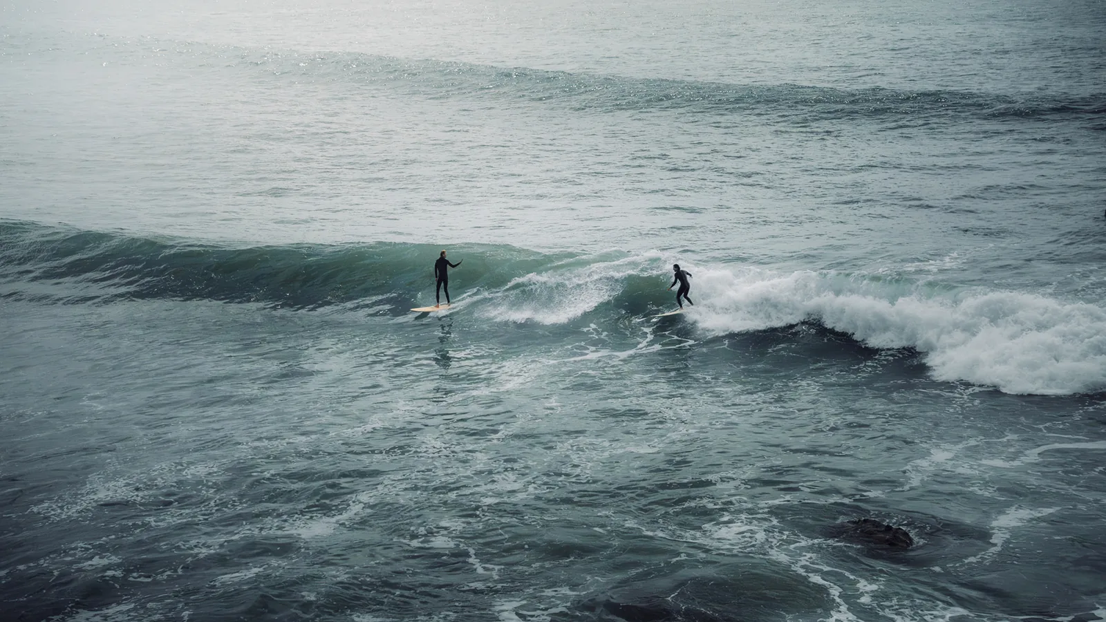A surfer paddles out while another rides a wave nearby off Essaouira, Morocco