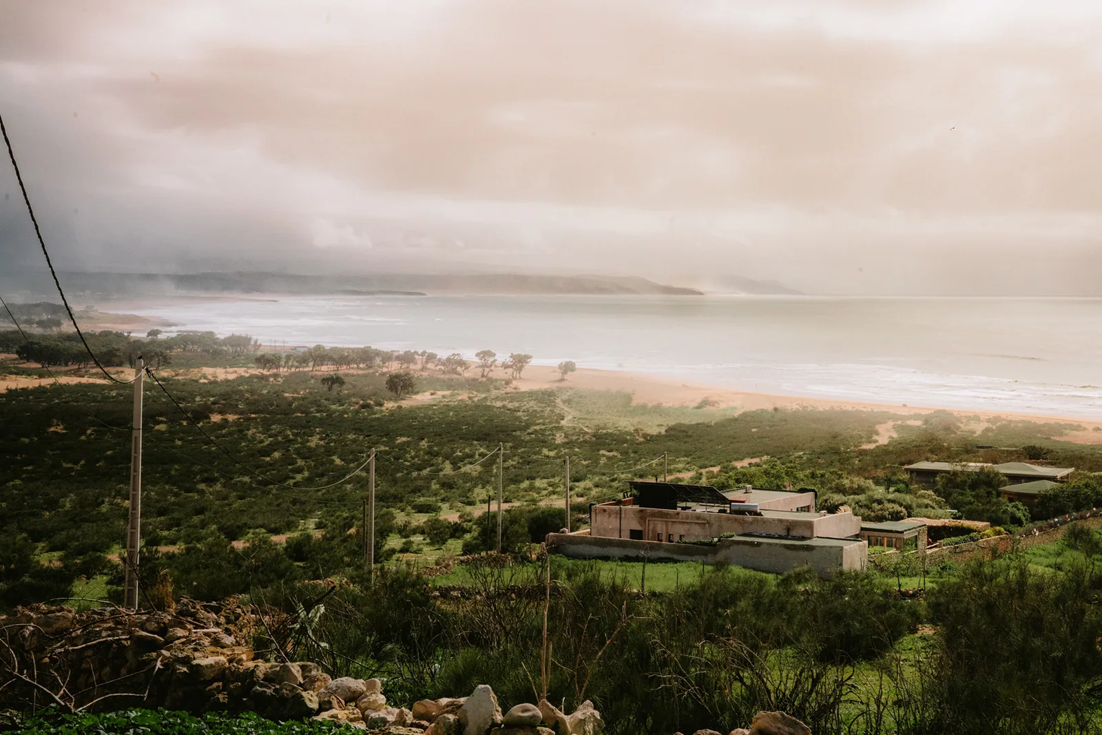 Mist rolls over a coastal village and beach seen from a hillside near Essaouira, Morocco
