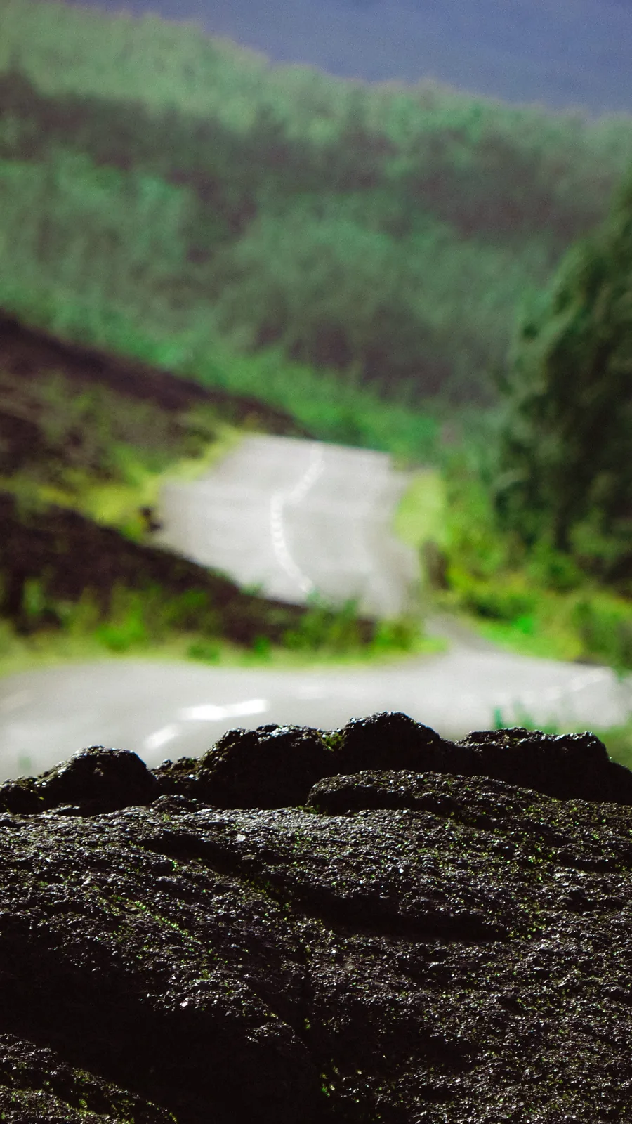 Blurred mountain road seen past a jagged lava rock foreground on Reunion Island