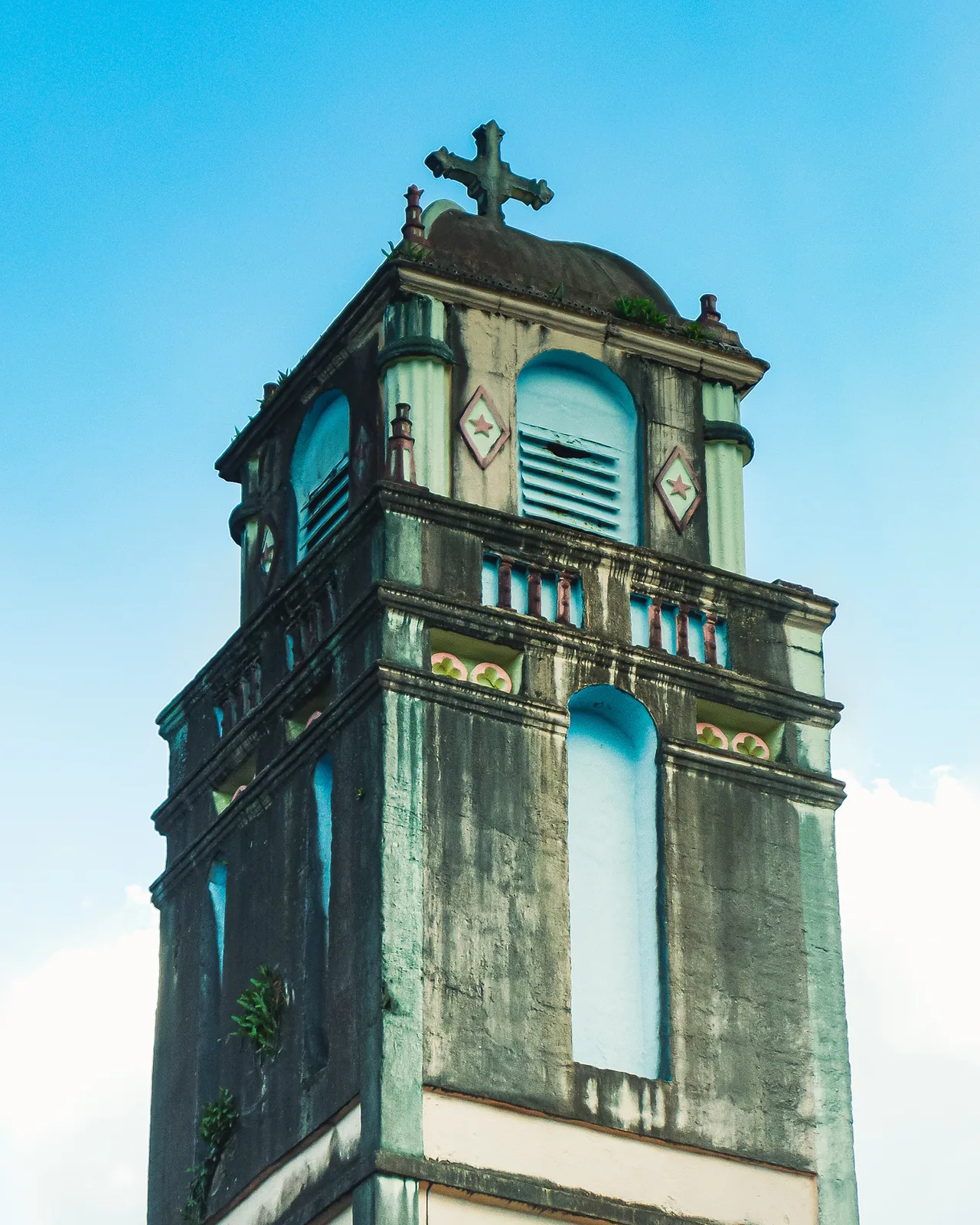 Weathered stone bell tower topped with a cross under a clear sky on Reunion Island