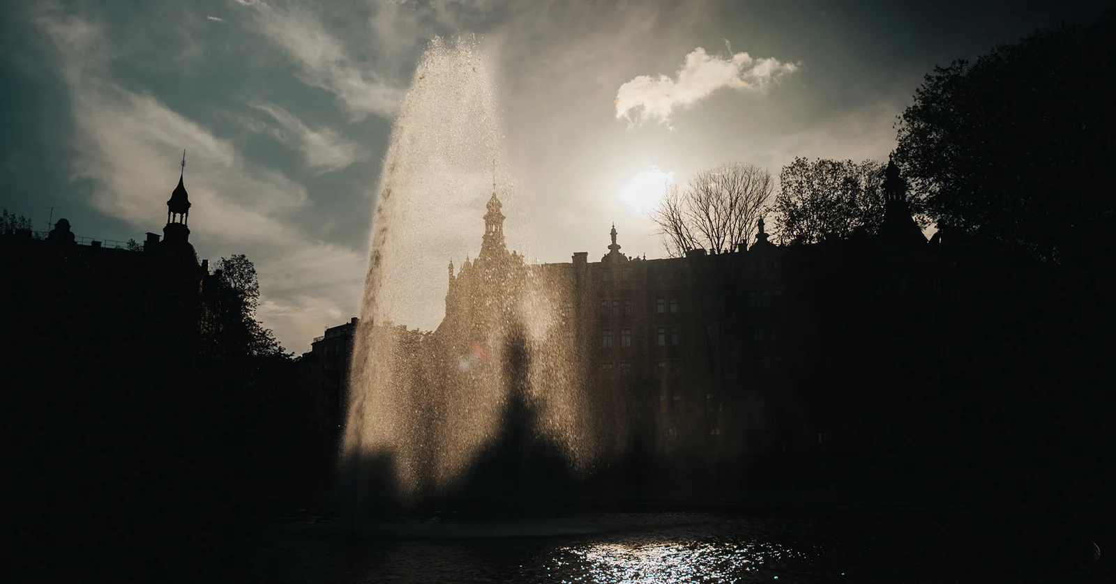 Fountain spray catching the sun before silhouetted city towers in Sweden