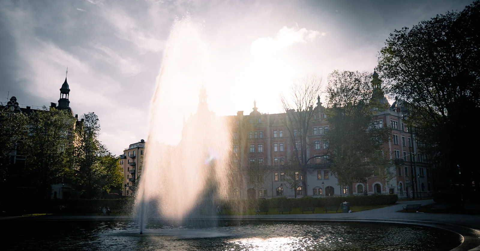 Tall fountain jet glowing against a historic city skyline in Sweden