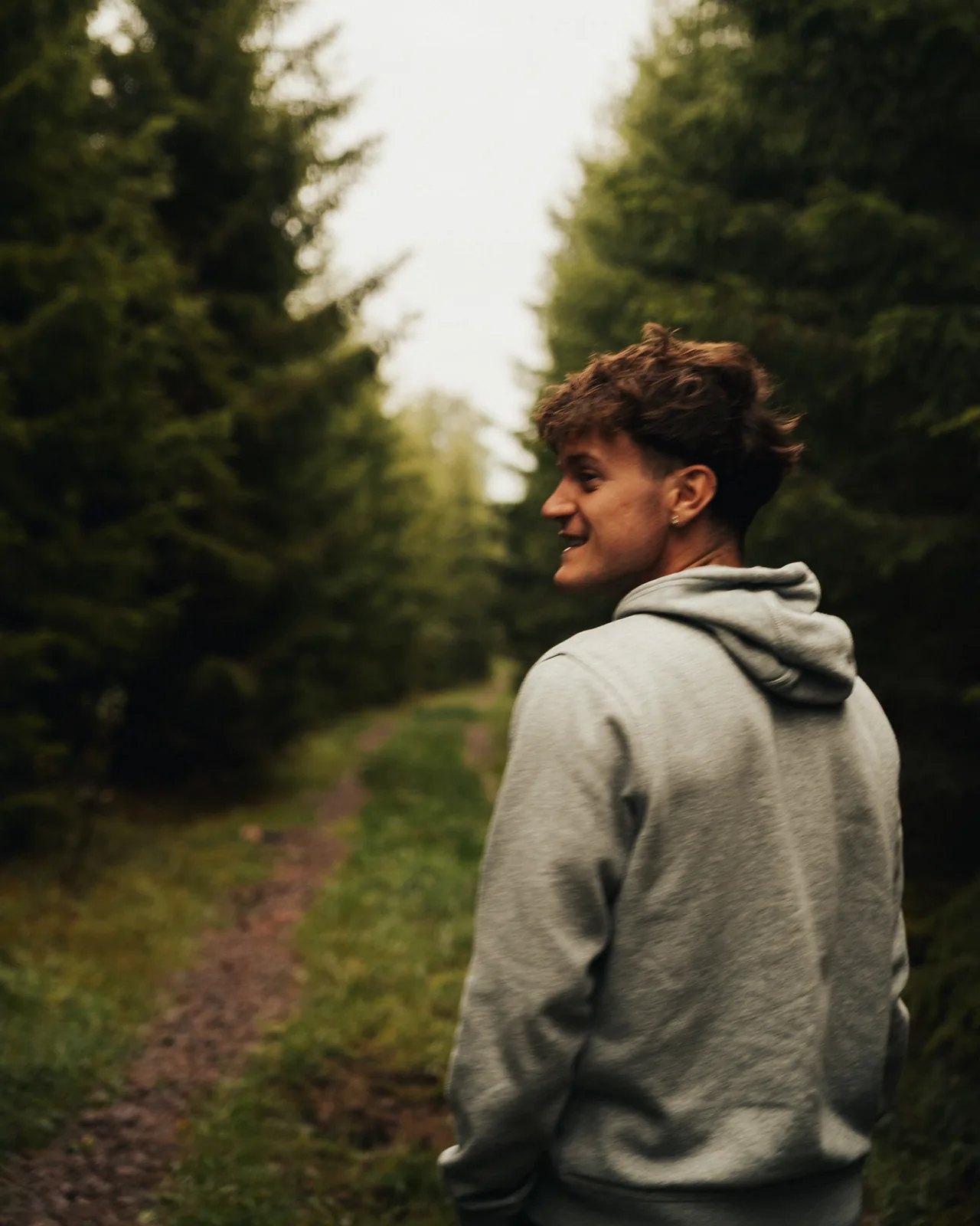 Young man glancing back with a smile along a forest trail among tall pines in Sweden