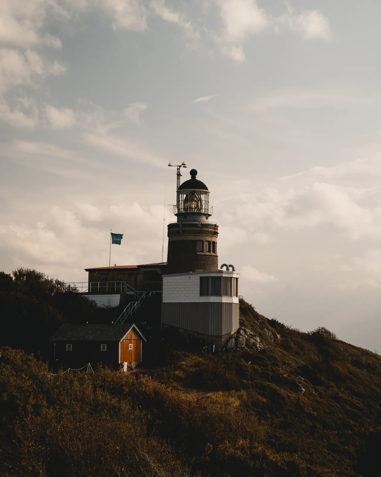 Lighthouse tower rising above a small orange cottage on a coastal hillside in Sweden