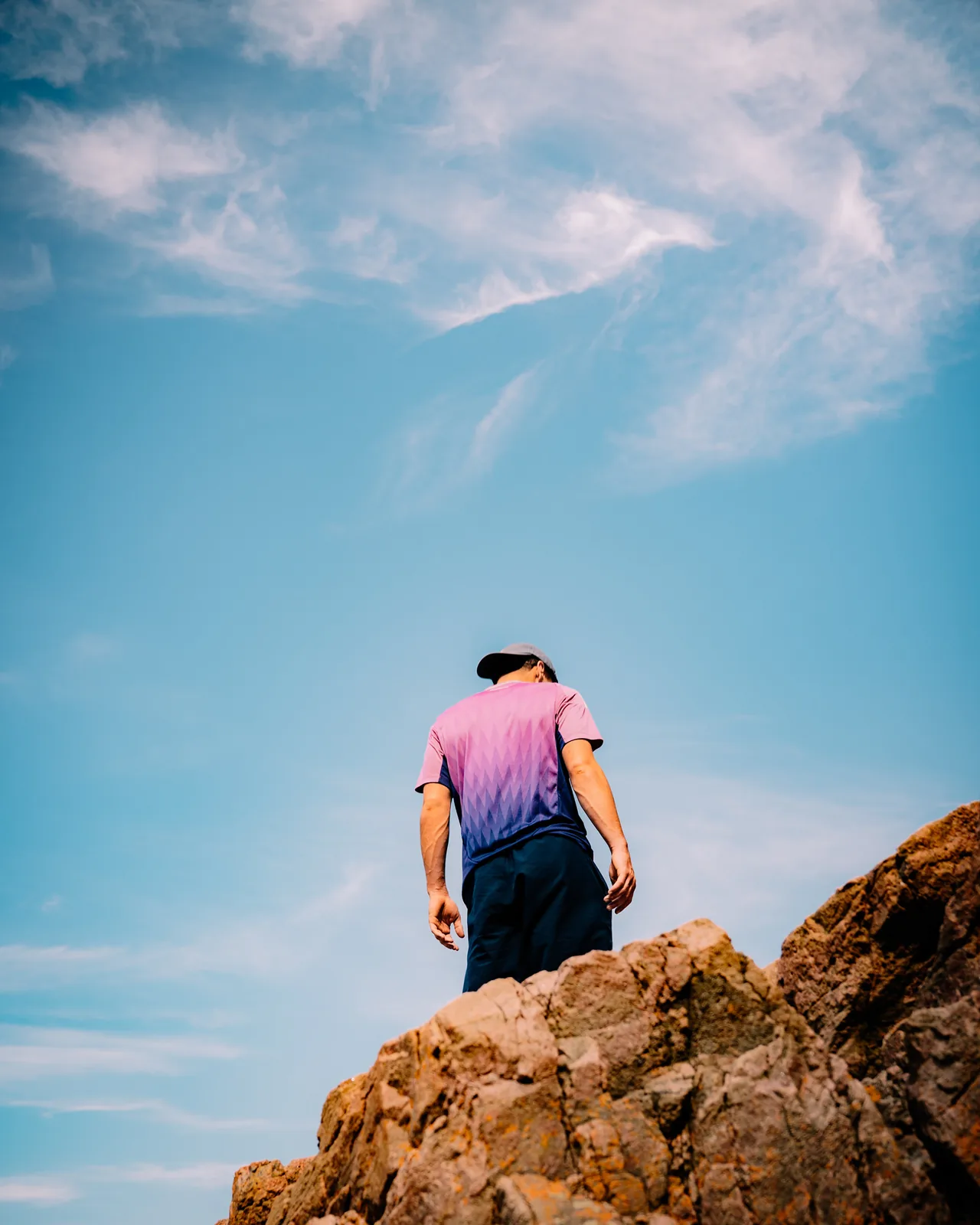 Man standing atop a rocky outcrop gazing up at a wispy sky in Sweden