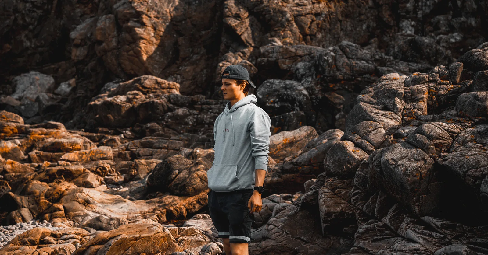 Man pausing among lichen-covered boulders on a rugged coastline in Sweden