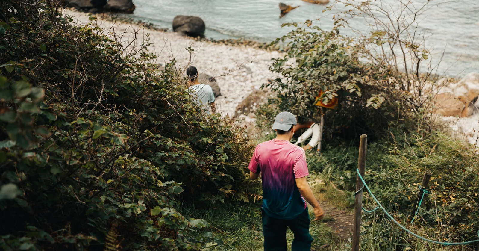 Friends making their way down a shrubby path toward a pebble beach in Sweden