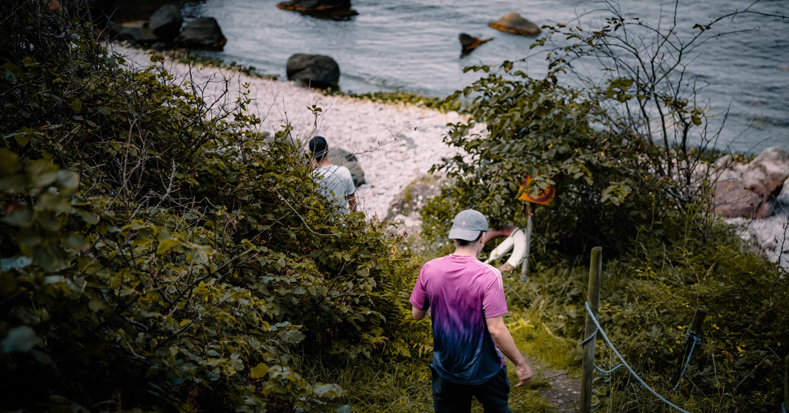 Group descending a narrow trail toward a rocky shoreline in Sweden