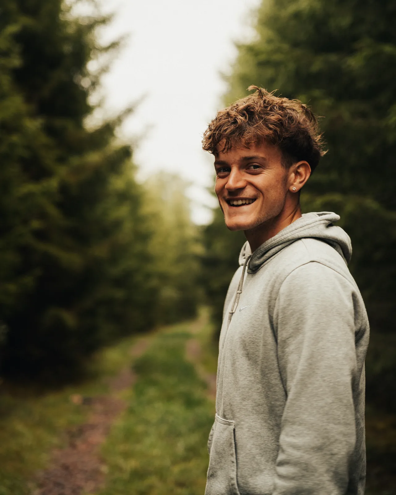 Smiling young man pausing on a forest path lined with pines in Sweden
