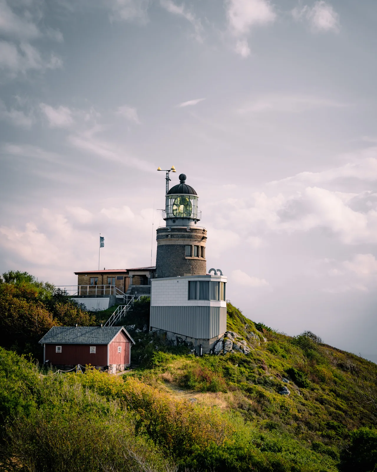 Lighthouse perched on a green hillside beneath a cloudy sky in Sweden