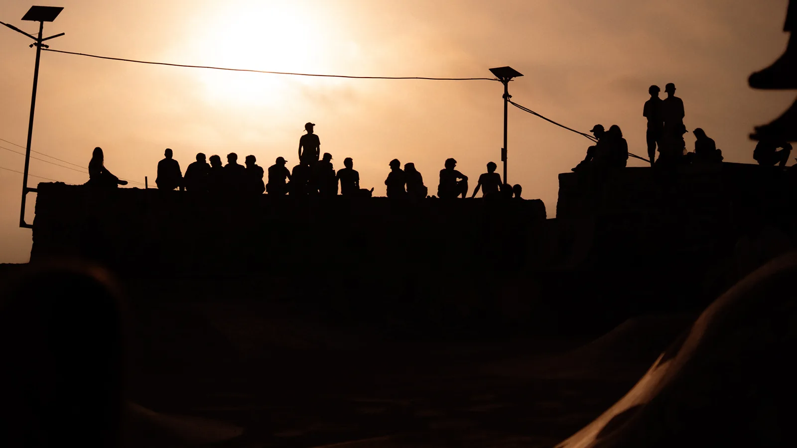 Spectators are silhouetted along a ledge against a glowing sunset in Taghazout, Morocco