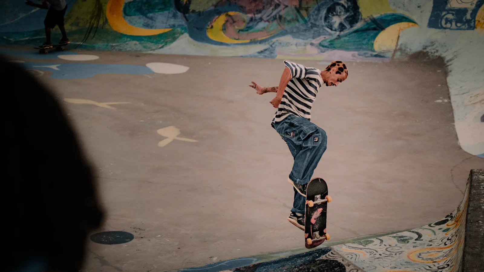 A skater in a striped shirt pops a trick inside a concrete bowl in Taghazout, Morocco