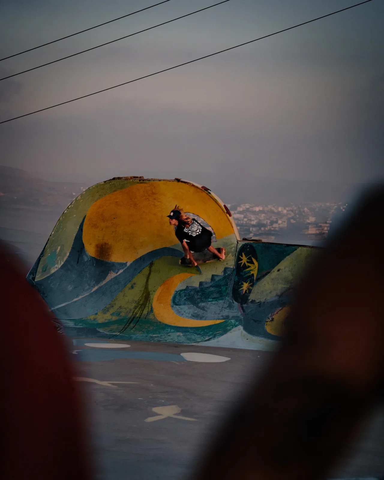 A skater rides a wave-painted ramp above the village rooftops at dusk, Taghazout, Morocco