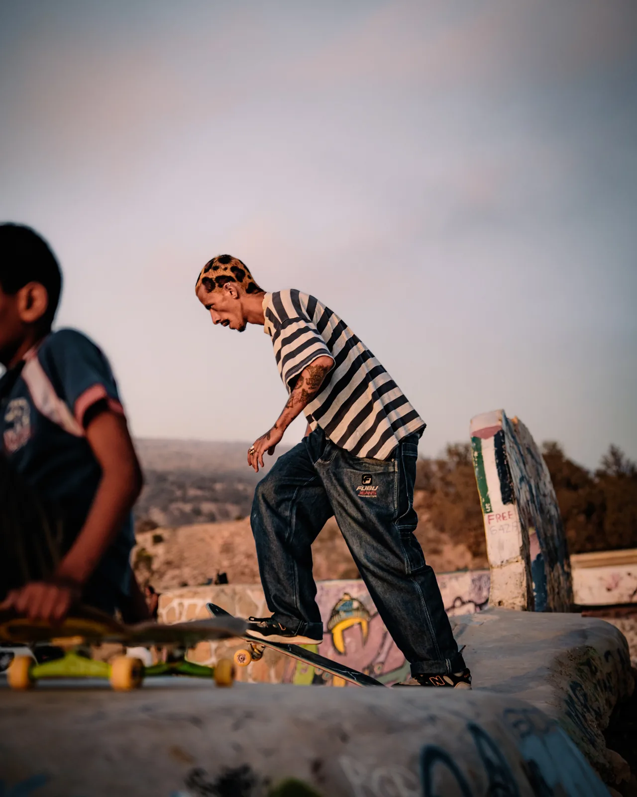 A skater in jeans and a striped shirt drops into a colourful bowl in Taghazout, Morocco