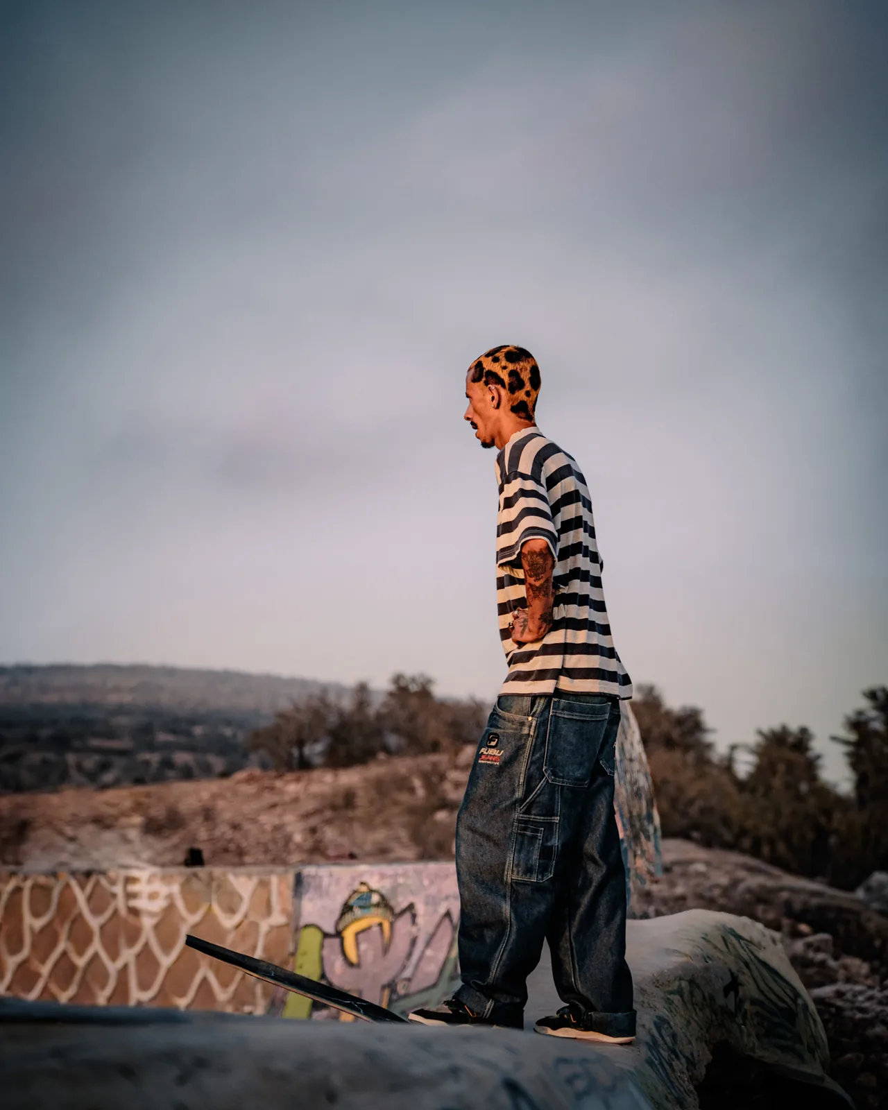 A skater pauses one-footed at the bowl's edge overlooking the hills of Taghazout