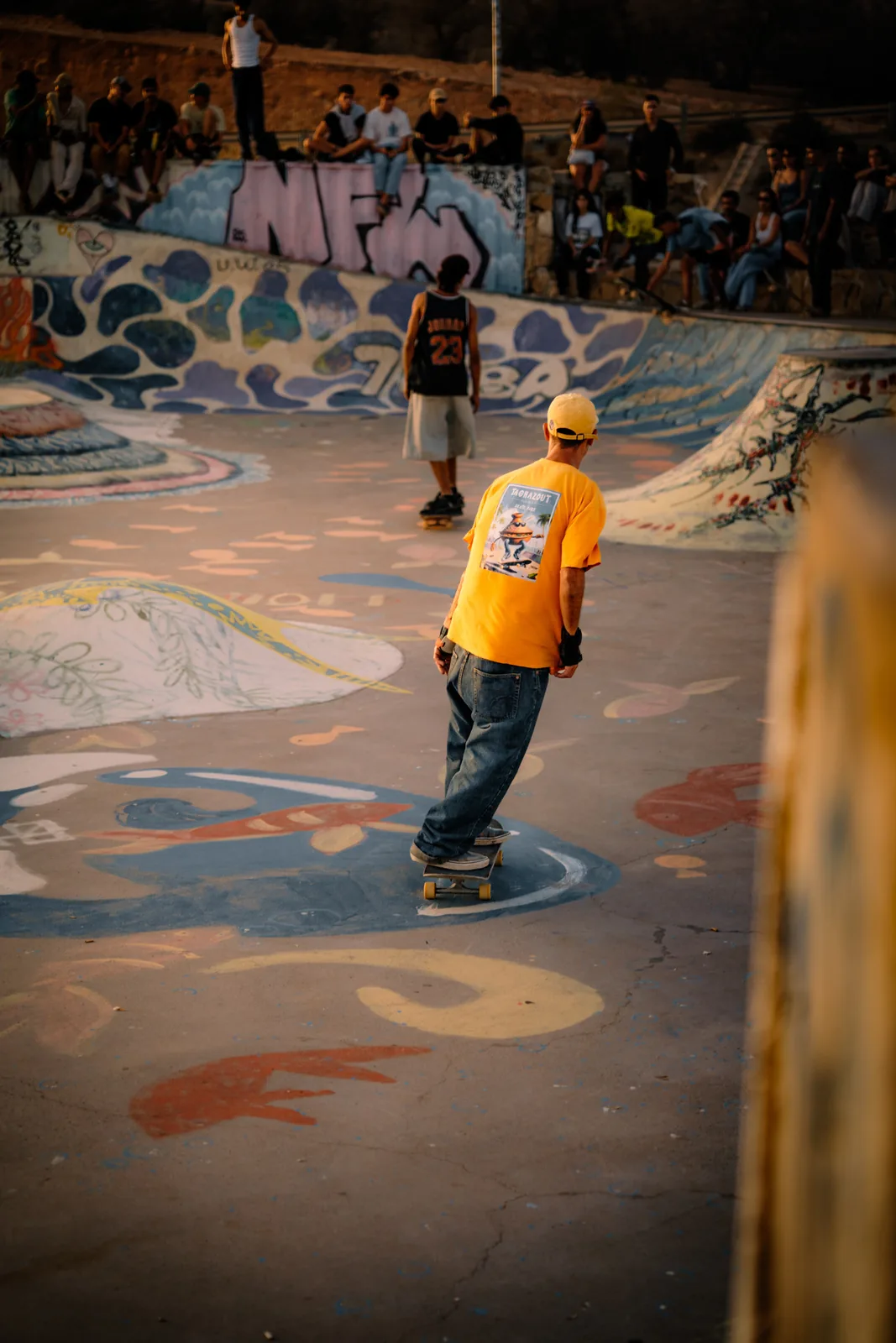 A skater in a yellow shirt cruises past a mural as onlookers watch in Taghazout, Morocco