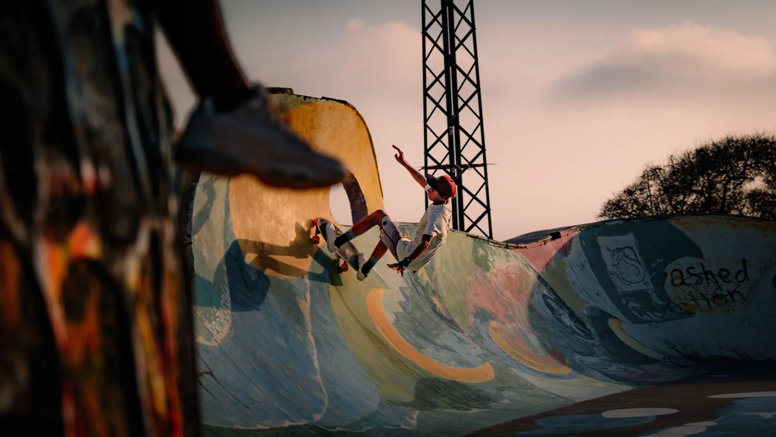 A skater grabs his board mid-trick with a steel tower glowing behind him, Taghazout