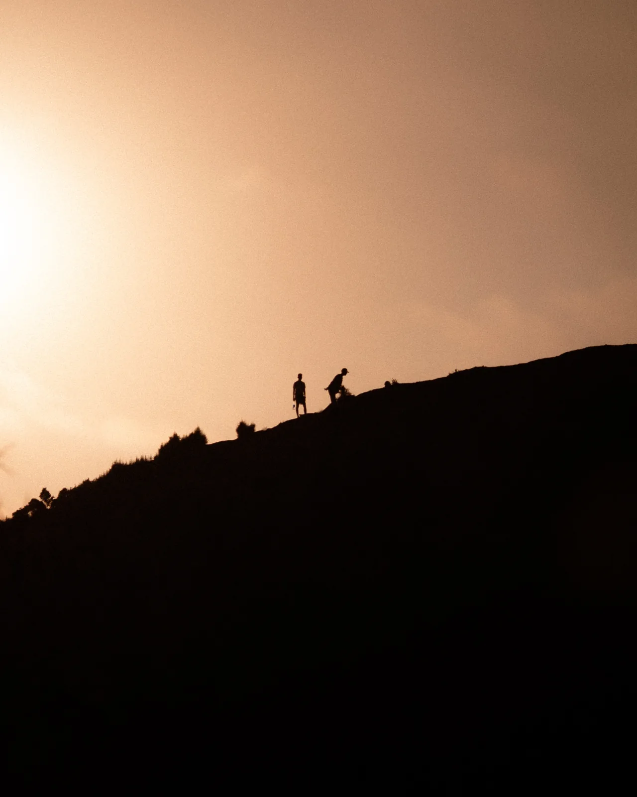 Small silhouetted figures walk a ridge at sunset above the hills near Taghazout, Morocco