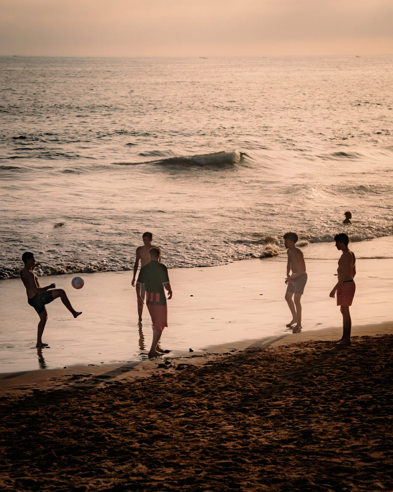 Boys playing football along the shoreline as gentle waves catch the evening light in Taghazout