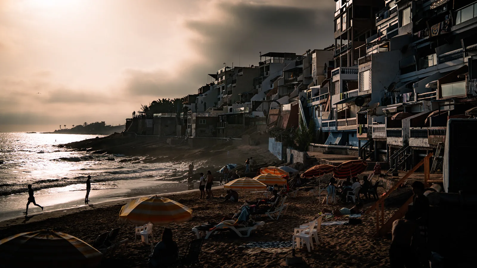 Terraced guesthouses and beach parasols overlook the shore at dusk in Taghazout, Morocco