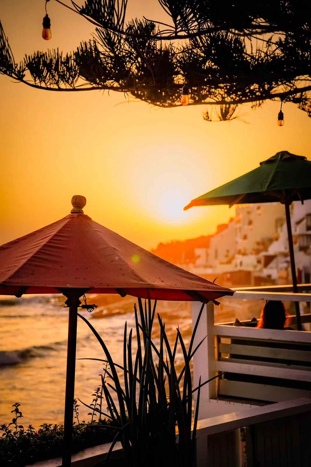 Red parasol silhouetted against a fiery sunset over the village of Taghazout, Morocco